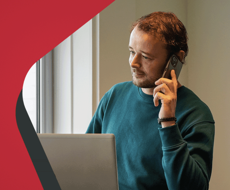 Mann telefoniert am Schreibtisch und arbeitet am Laptop